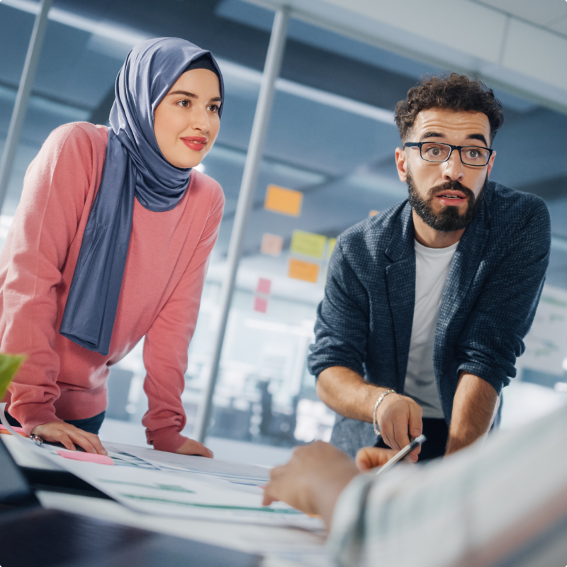 a Woman and a Man Leaning over a Desk Talking About a Project